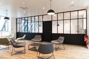 Espace de travail moderne aux murs en cloisons vitrées, équipé de chaises noires, offrant une atmosphère sophistiquée.